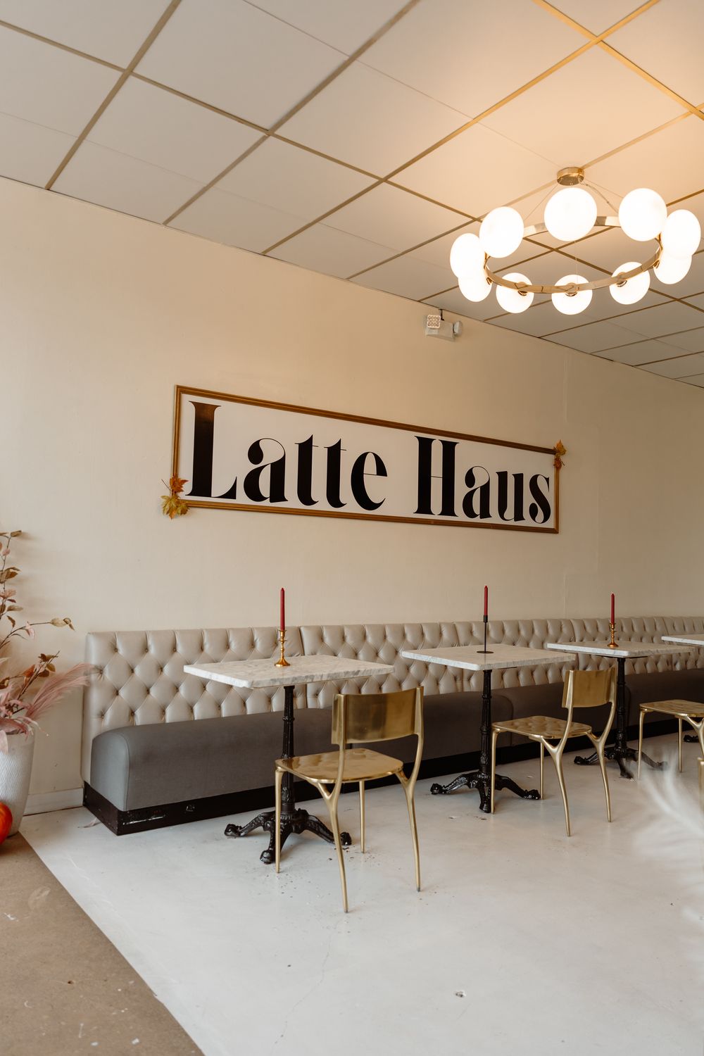 Inside Latte Haus: the gold Latte Haus sign over a tufted banquette, marble tables and a globe chandelier